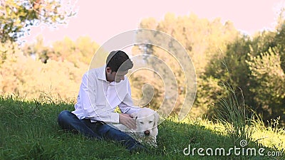 Hombre joven con el perro viejo de Labrador en la naturaleza almacen de metraje de vídeo Hombre joven con el perro viejo de Labrador en la naturaleza almacen de metraje de vídeo