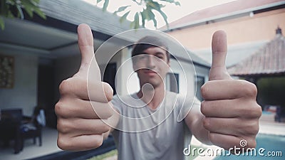 Hombre joven feliz que da dos pulgares para arriba y sonrisa al aire libre delante de la casa almacen de video Hombre joven feliz que da dos pulgares para arriba y sonrisa al aire libre delante de la casa almacen de video