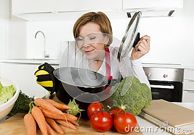 Home cook woman in red apron at domestic kitchen holding cooking pot with hot soup smelling vegetable stew Stock Photo