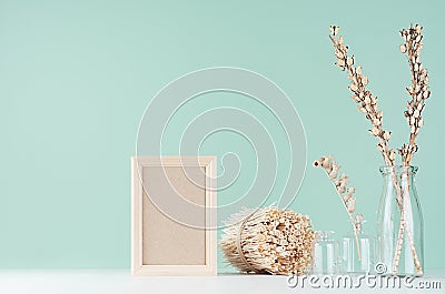 Home decor in eco style - blank photo frame, dried plants, twigs in glass bottle, twigs bunch in green mint menthe color interior. Stock Photo