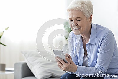 Home leisure for seniors. Happy elderly woman using smartphone at home Stock Photo