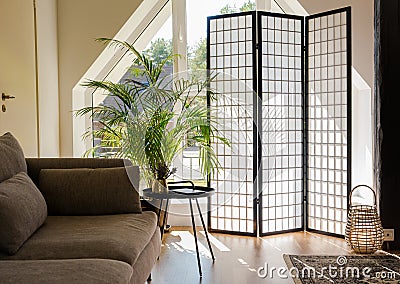 Home living room with wood and paper divider screen blocking sun from window, black metal accent table and sofa. Stock Photo