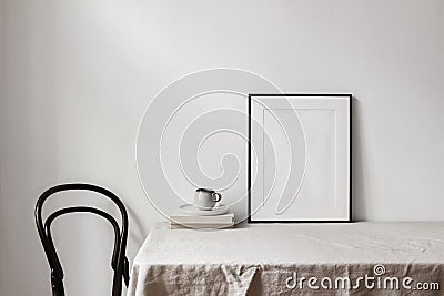 Home office concept. Empty black vertical picture frame mockup. Cup of coffee on old books, linen table cloth. White Stock Photo