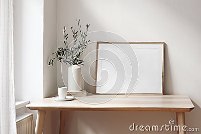 Home office concept. Empty horizontal wooden picture frame mockup. Cup of coffee on wooden table. White wall background Stock Photo