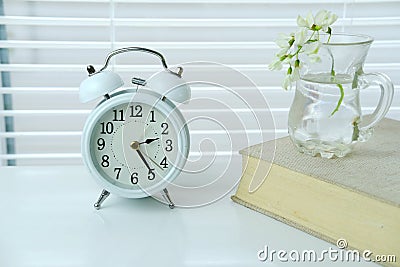 Home office table with white alarm clock, book and flower on blinds background, 2:30 pm, of a deadline, be in time, finish things Stock Photo