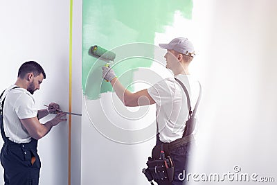 Home renovation worker with a tool belt painting a wall green wi Stock Photo