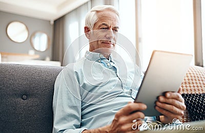 In the home zone with some wifi. a senior man relaxing and using a tablet on the sofa at home. Stock Photo