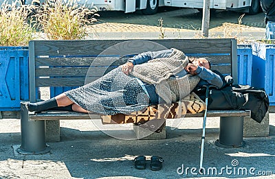 Homeless barefooted woman sleep on the wooden bench on urban street in the city on the sidewalk Stock Photo