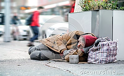 Homeless beggar man lying on the ground outdoors in city asking for money donation. Stock Photo