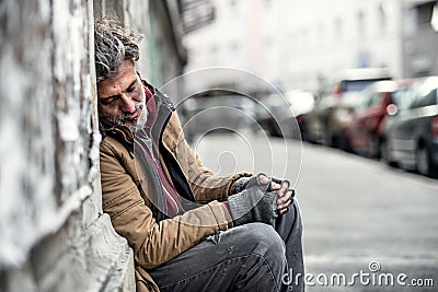 Homeless beggar man sitting outdoors in city asking for money donation, sleeping. Stock Photo