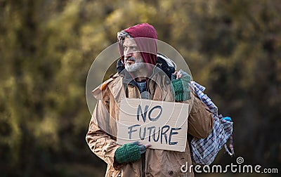 Homeless beggar man standing outdoors in park, holding bag and cardboard sign. Stock Photo