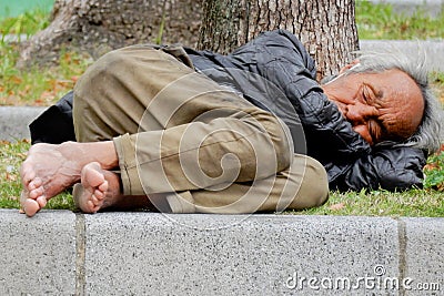 Homeless male sleeping under a tree barefoot Editorial Stock Photo