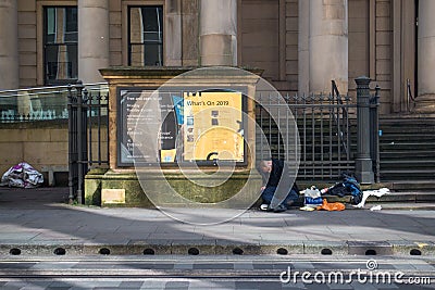 Homeless man sleeps on the street outside a stone building beside a information poster Editorial Stock Photo