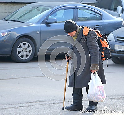 A homeless tramp with a stick walks through the Parking lot Editorial Stock Photo