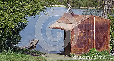 Homeless unemployed man made a hut for himself from an old abandoned linoleum from a dump on the lake Stock Photo