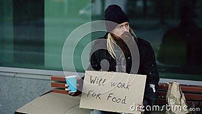 Homeless young man beg for money shaking cup to pay attention people walking near beggar at the city sidewalk Stock Photo