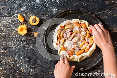 Homemade apricot galette made with fresh organic apricotes on wooden table, top view. Process of baking. Making dought. Hands with Stock Photo