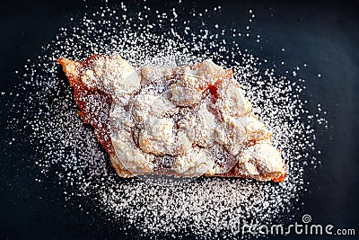 Homemade apricot pie. Top view of a slice of rustic hot sweet cake in icing sugar on a black plate. Natural organic food. Stock Photo