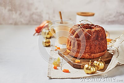 Homemade autumn carrot or pumpkin bundt cake with candied fruits, cup of tea and golden decorative pumpkins on light background Stock Photo