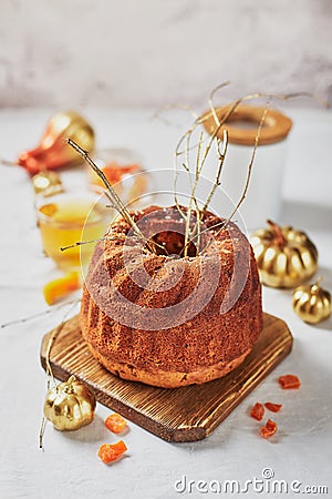 Homemade autumn carrot or pumpkin bundt cake with candied fruits, cup of tea and golden decorative pumpkins on light background Stock Photo