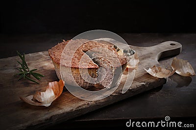 Homemade, baked meat pate. Rustic composition with cut pate on a wooden chopping board, on a black background. Stock Photo