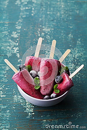 Homemade blueberry ice cream or popsicles decorated green mint leaves on teal rustic table, frozen fruit juice Stock Photo