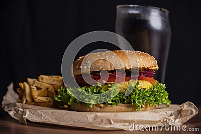 Homemade burger and french fries with oregano and frozen glass a tasty soda. Humburger served on pergament paper and wooden board. Stock Photo