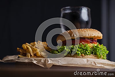 Homemade burger and french fries with oregano and frozen glass a tasty soda. Humburger served on pergament paper and wooden board. Stock Photo