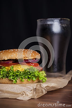 Homemade burger and french fries with oregano and frozen glass a tasty soda. Humburger served on pergament paper and wooden board. Stock Photo