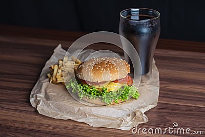 Homemade burger and french fries with oregano and frozen glass a tasty soda. Humburger served on pergament paper and wooden board. Stock Photo