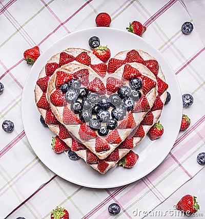 Homemade cake with Strawberries and blueberries for Valentine's Day heart shaped on a white plate on a striped tablecloth with sca Stock Photo