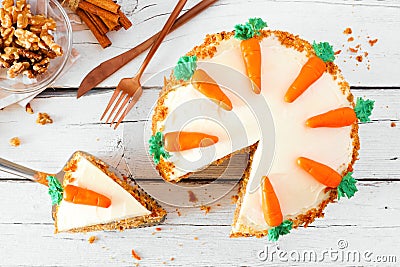 Homemade carrot cake with cream cheese frosting and slice being removed, above view table scene over white wood Stock Photo