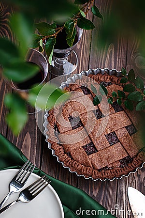 Homemade chocolate berry fruit pie on wooden background with green leaves, summer pie outdoors Stock Photo