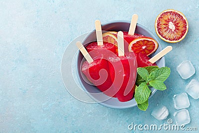 Homemade citrus ice cream or popsicles decorated mint and orange slices on blue table from above. Frozen fruit juice. Stock Photo