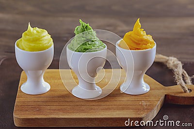 Homemade creamy multi coloured of mash potato in three eggcups in wooden plate and table. Stock Photo