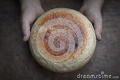 Homemade crusty loave of bread on wooden background. Baker holding fresh bread in the hands. view from above. Dark mood Stock Photo