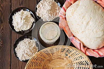 Homemade dough, sourdough in a jar, mix of flours, bread and basket for proof and spatula on a wooden background. Baking concept. Stock Photo