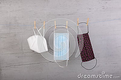 Homemade face mask, ffp2 mask and a medical mask hanging on a clothesline, fixed with clothespins, white wooden board as Stock Photo