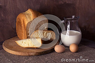 Homemade fresh bread, milk in a jug and eggs on a wooden table. Stock Photo