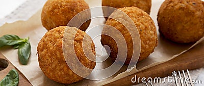 Homemade fried Arancini with basil on a rustic wooden board, low angle view. Italian rice balls. Close-up Stock Photo