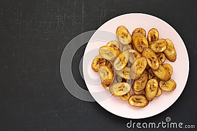 Homemade fried plantains on a pink plate on a black surface, overhead view. Flat lay, from above, top view. Copy space Stock Photo