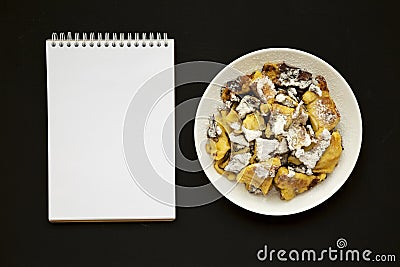 Homemade german Kaiserschmarrn pancake and blank notepad on a black background, top view. Flat lay, overhead, from above. Copy Stock Photo