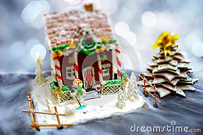 Homemade gingerbread house, gingerbread Christmas tree and a sugar mastic snowman on background of defocused silver lights Stock Photo