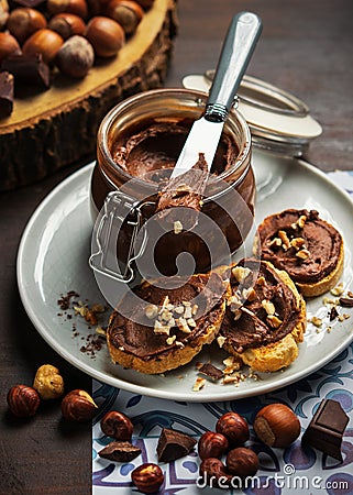 Homemade hazelnut cream in bowl with hazelnut nuts and slices of toast with chocolate cream on wooden background Stock Photo