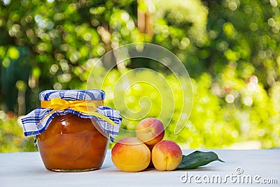 Homemade jam on a green natural background. A jar of home apricot jam and fresh apricots on a white table. Stock Photo