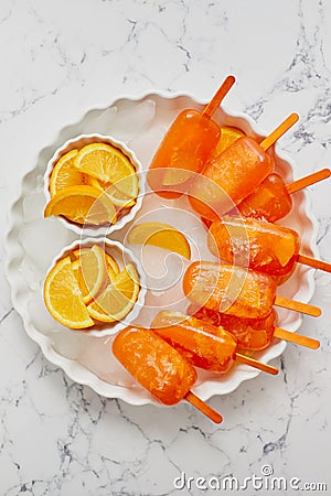 Homemade, juicy, orange popsicles. Placed on a white plate with ice cubes Stock Photo