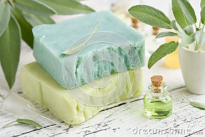 Homemade natural organic soap bars, bottle of essential sage oil and fresh green sage leaves on white table Stock Photo