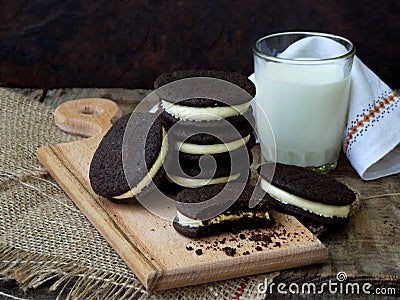 Homemade Oreo chocolate cookies with white marshmallow cream and glass of milk on dark background. Stock Photo