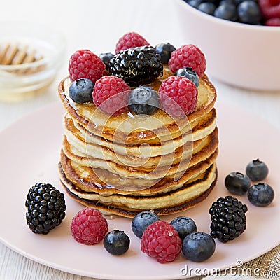 Homemade pancakes with berries and honey on a pink plate, side view. Close up Stock Photo