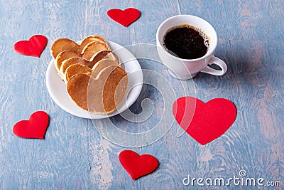 Homemade pancakes in the shape of a heart on a white plate, a mug with coffee or cocoa on a blue background Stock Photo